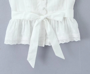 Détail de la taille du haut blanc avec nœud, boutons en tissu et ourlet en dentelle