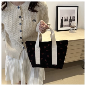 Detail of black corduroy tote bag with red strawberry pattern and cream woven handles