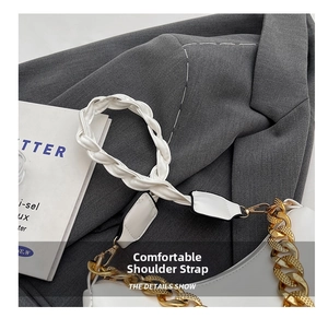 Detail of white leather shoulder bag featuring woven strap and gold chain accessory