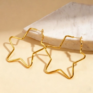 Detail of minimalist gold hollow star hoop earrings resting on white marble surface