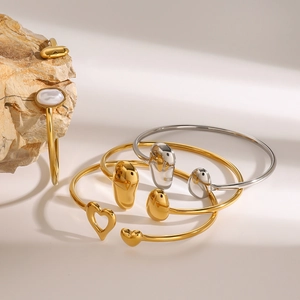 Detail minimalistischer Gold- und Silberarmreifen mit Muscheleinlage und Tropfenanhänger