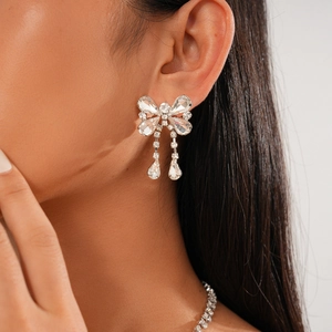 Detail of silver bow earrings with sparkling rhinestones and teardrop tassels on model