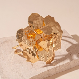 Detailed view of oversized metallic gold flower cuff bracelet on a sandstone pedestal