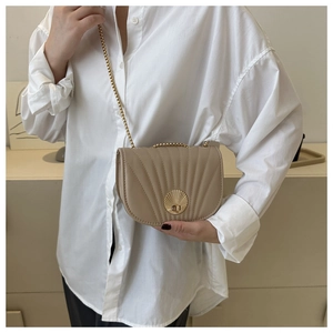 Detail of elegant beige saddle bag featuring shell lock and quilted pattern on white shirt