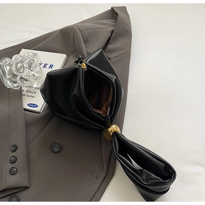 Detail of black PU leather triangular handbag featuring a gold ball charm and zip opening