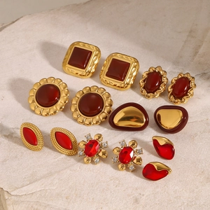 Collection of vintage gold-plated earrings with red gemstones on stone surface
