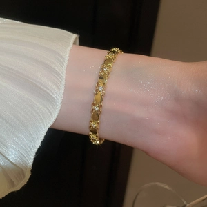Close-up of 18k gold plated cuff bracelet with heart and zircon clover charms on wrist