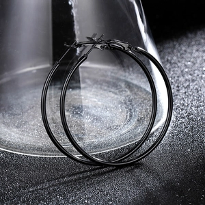 Minimalist black oversized metal hoop earrings with a semi-matte finish on dark texture