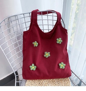 Detail of red canvas tote bag with green crochet floral accents on a chair