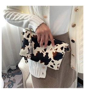 Detail of cow print envelope clutch featuring long black tassel and metal zipper