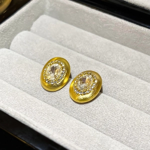Macro shot of oval gold brushed metal earring with a large gemstone and pavé accents