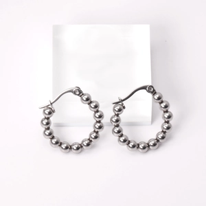 Macro detail of silver stainless steel beaded hoop earrings on a white display pedestal