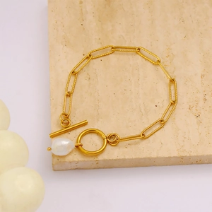 Dettaglio del bracciale dorato con perla barocca e chiusura OT su base in pietra beige