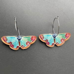 Macro detail of colorful butterfly earrings with turquoise wings and silver metal hoops