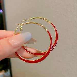 Macro shot of large red enamel and gold hoop earrings showing glossy finish details