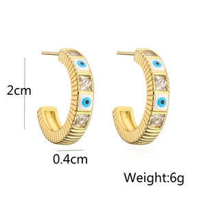 Detail view of C-shaped gold-plated earrings with white zircon and blue evil eye enamel
