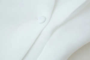 Detailed close-up of white blazer fabric texture and refined fabric-covered buttons