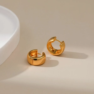 Detailed close-up of small thick gold-plated hoop earrings with a polished finish