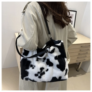 Close-up of a large faux fur cow print tote bag with black leather shoulder straps