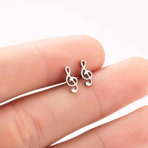 Macro shot of silver music note stud earrings on a fingertip showing delicate size details