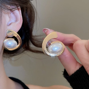 Detailed close-up of golden oval tassel earrings with large white pearls worn by a model