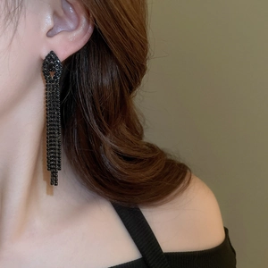 Detailed view of long black tassel earrings with crystals worn by a model on an olive background