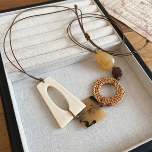 Detailed macro view of geometric rattan pendant necklace with wooden beads and leather cord