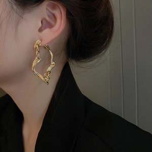 Elegant gold twisted geometric hoop earrings with striped texture shown on a female model