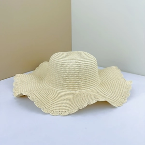 Detail of a beige straw beach hat featuring a wavy scalloped edge and woven texture