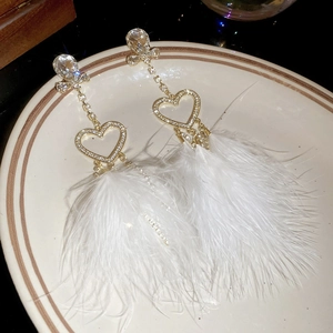 Close-up of gold tassel earrings with crystal heart and white feather fringe on ceramic tray