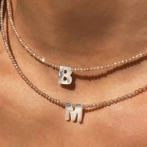 Close-up of beaded necklace with mother of pearl letters B and M on champagne beads