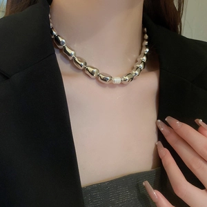 Close-up of irregular silver metal beads choker featuring a central white pearl on neck