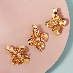 Three gold flower hair clips with rhinestones on a soft pink and blue background