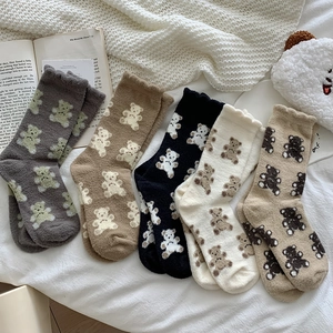 Five pairs of coral fleece bear socks in neutral colors laid on a cozy white bedsheet