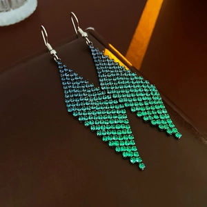 Détail macro de boucles d'oreilles pampilles à strass dégradé bleu vert sur cuir
