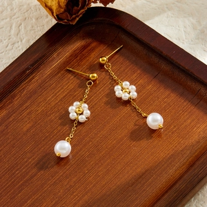 Détail de boucles d'oreilles chaînes dorées avec fleurs de perles sur plateau