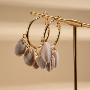 Detail shot of bohemian shell hoop earrings hanging on a gold metal jewelry display stand