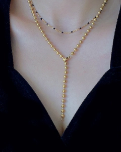 Detail of a layered golden Y-necklace featuring black beads and metallic drop pendant