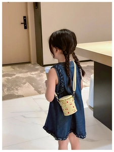 Detail view of a beige cylinder cherry print crossbody bag worn by a young girl