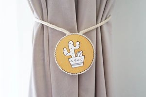 Detail of wooden magnetic curtain tieback with hand-painted cactus on beige rope