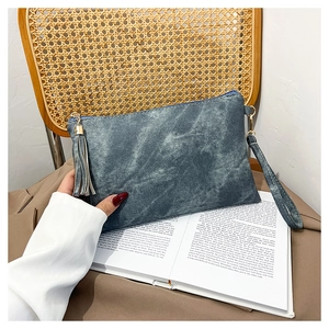 Blue-gray vintage textured clutch bag with a wrist strap and fringe tassel on an open book