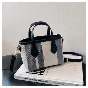 Detail of grey striped woven tote bag with black leather handles and gold metal hardware
