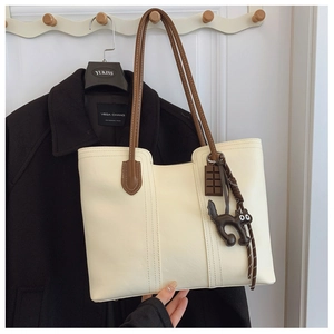 Detail of cream tote bag featuring brown handles and cute cat leather pendant