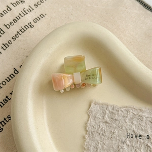 Detailed top view of a marbled peach and green acetate bow hair claw on a ceramic tray