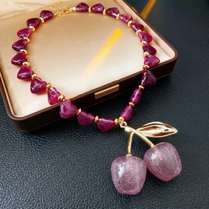 Acrylic purple heart beaded necklace with oversized cherry pendant on leather background