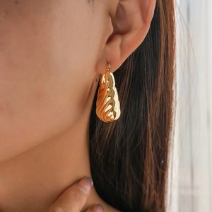 Close-up of golden geometric textured hoop earrings worn by a model in a minimalist style
