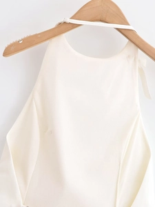 Detail of cream halter top with delicate straps hanging on a wooden hanger