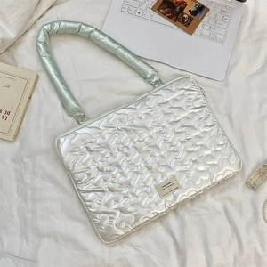 Flat lay of heart-quilted laptop sleeve in pearl white on aesthetic fabric background