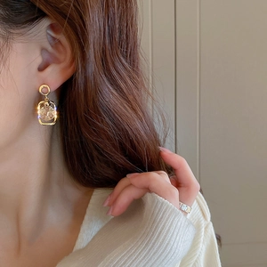 Close-up of geometric gold earrings with clear gemstones on model with ring accessory