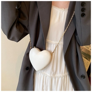 Close-up of white heart-shaped mini crossbody bag with gold chain strap on model